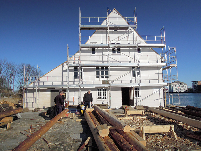 Bergesenhuset. Sørfasaden under restaurering. På kaien foregår tilhogging av nye stolper, bjelker og sperr.